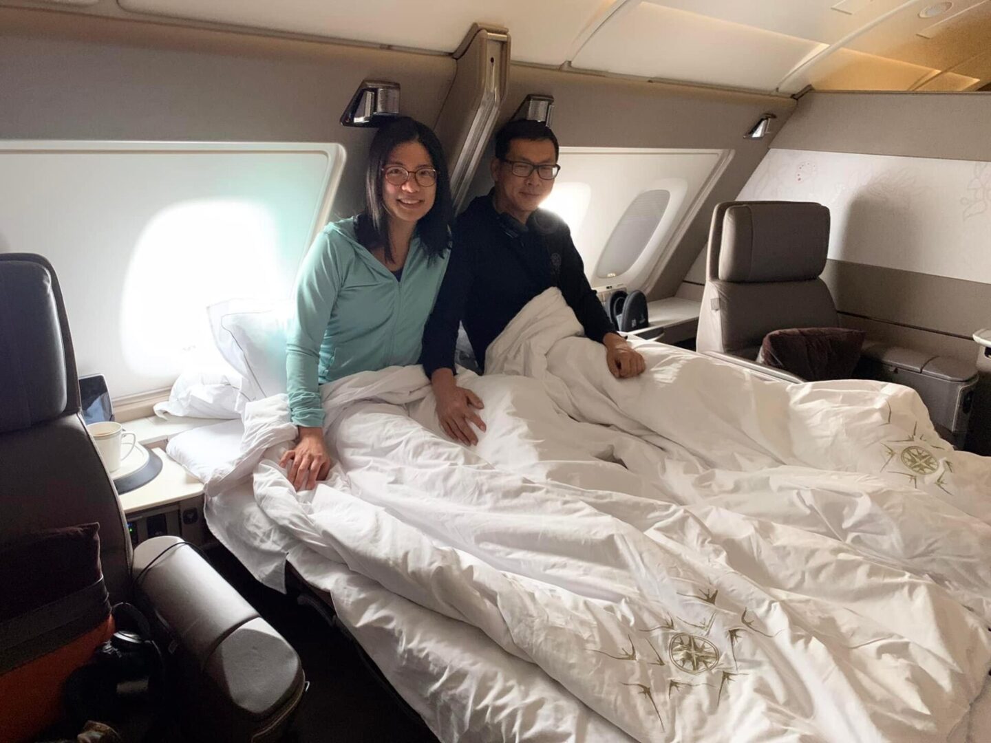 Two people are sitting on a bed in an airplane.